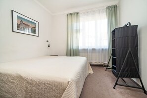 A hotel room with a bed, a picture on the wall, a window with curtains, and a storage unit.