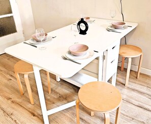 A white dining table with four chairs, each with a wooden seat and backrest. The table is equipped with a black center console and has a white drawer unit on one side. - Clean apartment easy location (Praha 3)