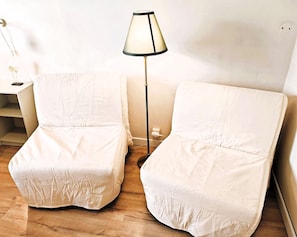 Two white chairs with a cushion, a floor lamp, and a white wall.