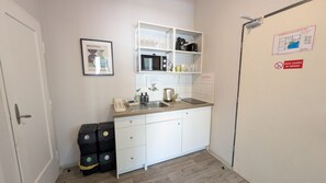 A compact kitchen with white cabinets, a microwave, and a sink. There are black trash bins and a framed picture on the wall. - Modern apartment Great location for 7 people (Praha)