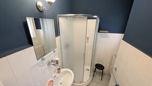 Une salle de bain avec une douche à parois de verre, un lavabo avec un miroir et un petit tabouret.