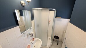 A bathroom with a glass-enclosed shower, a sink with a mirror, and a small stool.