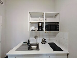 A compact kitchen with a sink, a stove, a microwave, and a coffee maker on the countertop.