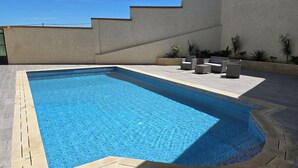 A rectangular swimming pool with a tiled edge, surrounded by a patio area with outdoor furniture and plants. - Villa Tangier vispless pool with panoramic sea view  (Tangier)