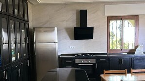 A modern kitchen with a curved island, dark cabinetry, stainless steel appliances, and a large window providing natural light. - Villa Tangier vispless pool with panoramic sea view  (Tangier)