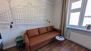 A room with a brown sofa, a small table, a lamp, and a wall mural.