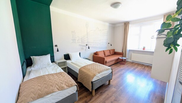 A hotel room with two beds, a sofa, a map on the wall, and a window with curtains.