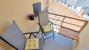 Un balcón con dos sillas, una mesita y un calentador de pared, con vista al techo del edificio.