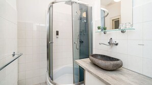 Un baño moderno con ducha acristalada, bañera independiente y lavabo de piedra.