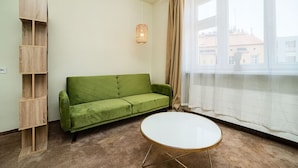 Una habitación con un sofá verde, una mesa redonda blanca y un estante de madera.