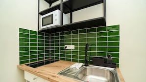 Una cocina con un lavamanos de acero inoxidable, un microondas y un salpicadero de azulejos verdes.