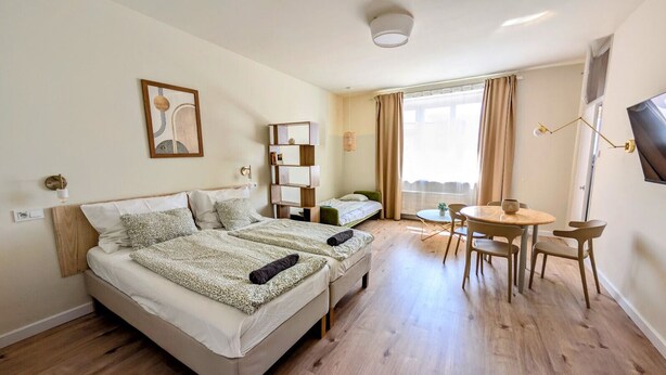 Una habitación de hotel con dos camas, una mesita con sillas, un televisor y una ventana con cortinas.
