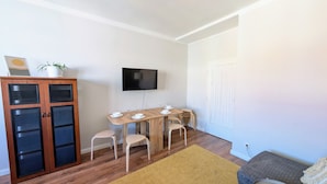 A living room with a wooden dining table, four chairs, a TV mounted on the wall, a cabinet with glass doors, and a door. - Compact Apartment Sleeps 6 + Great Location (Praha 3)