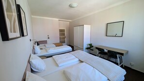 A hotel room with two single beds, a desk, a chair, and a wardrobe.