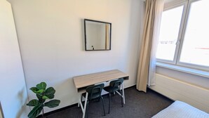 A room with a desk, two chairs, a mirror, a plant, and a window with curtains. - Compact Apartment Sleeps 6 + Great Location (Praha 3)