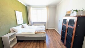 A bedroom with two beds, a wardrobe, a window with curtains, and a green wall.