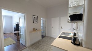 A modern kitchen with a wooden countertop, a kettle, and a microwave. There is a door leading to a hallway with a bench and a framed picture on the wall. - Compact Apartment Sleeps 6 + Great Location (Praha 3)