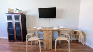 A dining area with a wooden table, six chairs, a television mounted on the wall, and a cabinet with a plant on top.