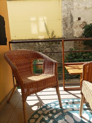 A wicker chair and a small table on a balcony with a view of a garden and a building wall. - Fun bright studio with flat screen TV (Prague)