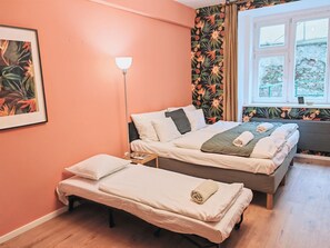 A bedroom with two beds, a bedside table, a floor lamp, and a window with a view of a stone wall and greenery outside. - Fun bright studio with flat screen TV (Prague)