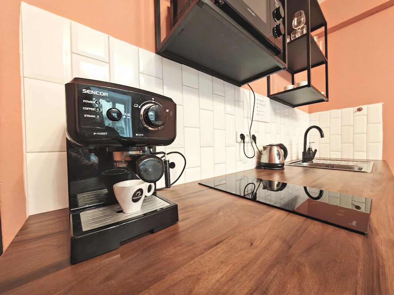 A modern kitchen with a black coffee machine, a kettle, and a sink.