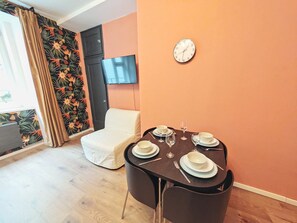 A dining area with a table set for four, a sofa, a TV, and a clock on the wall. - Fun bright studio with flat screen TV (Prague)