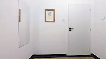 A hallway with a white door, a framed picture on the wall, and a mirror on the left.
