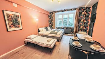 A room with two beds, a dining table with bowls, a painting, and a window with curtains.
