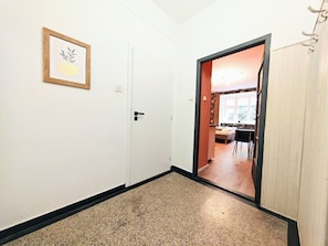 A hallway with a framed picture on the wall, a door leading to a room with a bed and a table, and a wooden door on the right. - Fun bright studio with flat screen TV (Prague)