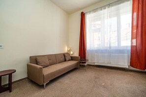 A small, furnished room with a sofa, a small table, and a window with curtains.