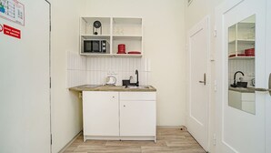 Cocina compacta con armarios blancos, microondas y lavamanos. A la derecha, una puerta con espejo.