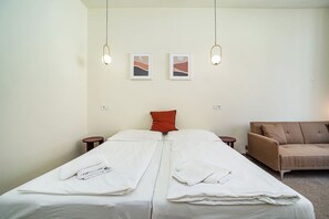 A double bed with white linens, a red pillow, and two bedside tables. There is a brown sofa and two framed pictures on the wall. - Modern, bright studio in a great location (Praha)