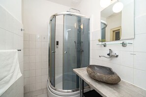 A modern bathroom with a glass shower enclosure, a stone sink, and a mirror with lights.