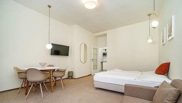 Una habitación moderna y bien iluminada con una cama, un sofá, una mesa de comedor con sillas y un televisor montado en la pared.