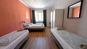 Une chambre d’hôtel avec deux lits simples, un grand lit, un miroir et une fenêtre avec des rideaux.