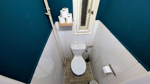 Une petite salle de bain avec des toilettes, un plancher en bois, des carreaux blancs et un mur bleu.