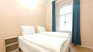 A bedroom with a bed, a nightstand, and a window with curtains.