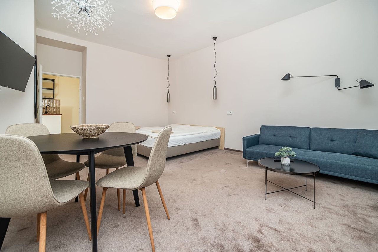 Ein modernes Wohnzimmer mit einer Couch, einem Esstisch mit Stühlen, einem Bett und einem kleinen Tisch mit einer Pflanze.