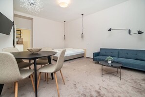A modern living room with a sofa, a dining table with chairs, a bed, and a small table with a plant.