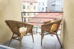 A balcony with two wicker chairs and a yellow cushion, overlooking a building with red roofs. - Modern studio with balcony + TV (Praha 3)