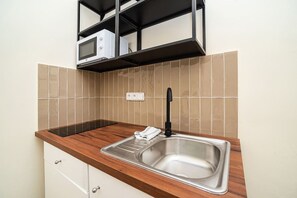 A kitchen with a stainless steel sink, wooden countertop, and a microwave on a shelf.