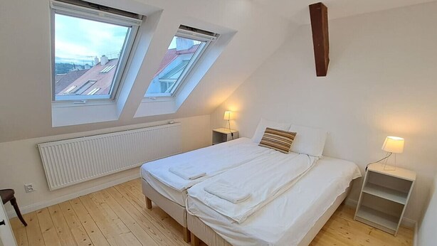 Une chambre avec deux lits, des fenêtres de toit, un radiateur et des tables de chevet avec des lampes.