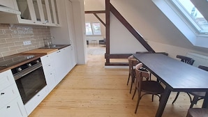 Une cuisine moderne avec des armoires blanches, un comptoir en bois et un four encastré. On y trouve également un coin repas avec une longue table et des chaises.