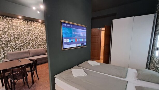 A modern hotel room with a large bed, a small desk, a sofa, and a TV mounted on the wall. - Chic+Contemporary Zizkov Studio (Praha 3)