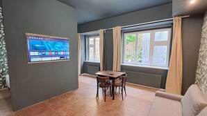 A room with a dining table and chairs, a TV mounted on the wall, and large windows with curtains. - Chic+Contemporary Zizkov Studio (Praha 3)