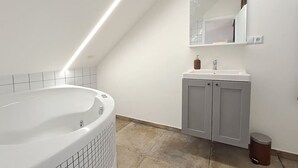 A modern bathroom with a freestanding bathtub, a vanity with a mirror, and a trash can. - Prague Urban Oasis Loft (Praha 2)