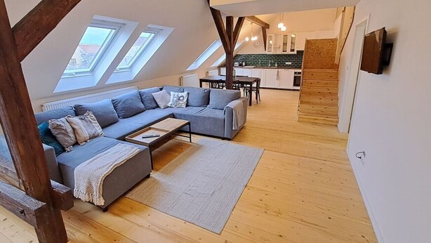 A modern loft apartment with a large gray sofa, a wooden dining table, and a kitchen in the background. - Prague Urban Oasis Loft (Praha 2)