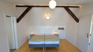 A bedroom with a wooden floor, a bed with a beige and blue bedspread, two bedside lamps, and a ceiling light fixture. - Prague Urban Oasis Loft (Praha 2)