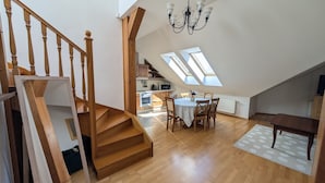 Un loft spacieux avec un escalier en bois, un coin repas comprenant une table et des chaises, et des fenêtres de toit qui laissent entrer la lumière naturelle.