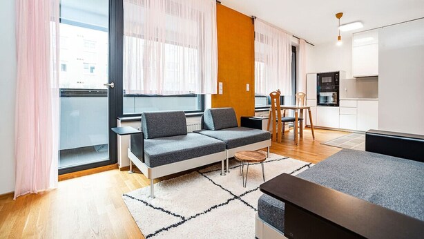 Ein modernes Wohnzimmer mit einer Couch, einem kleinen Tisch und einer Küchenzeile im Hintergrund.